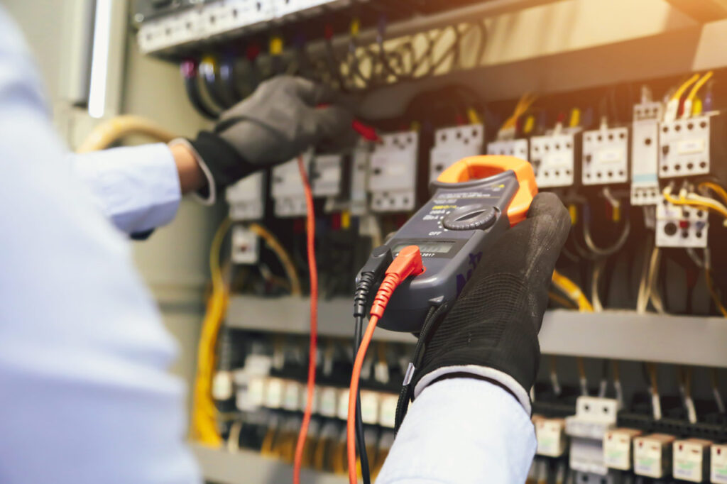 An electrician inspecting and testing circuit breakers with a clamp meter, ensuring electrical systems are safe and operational.