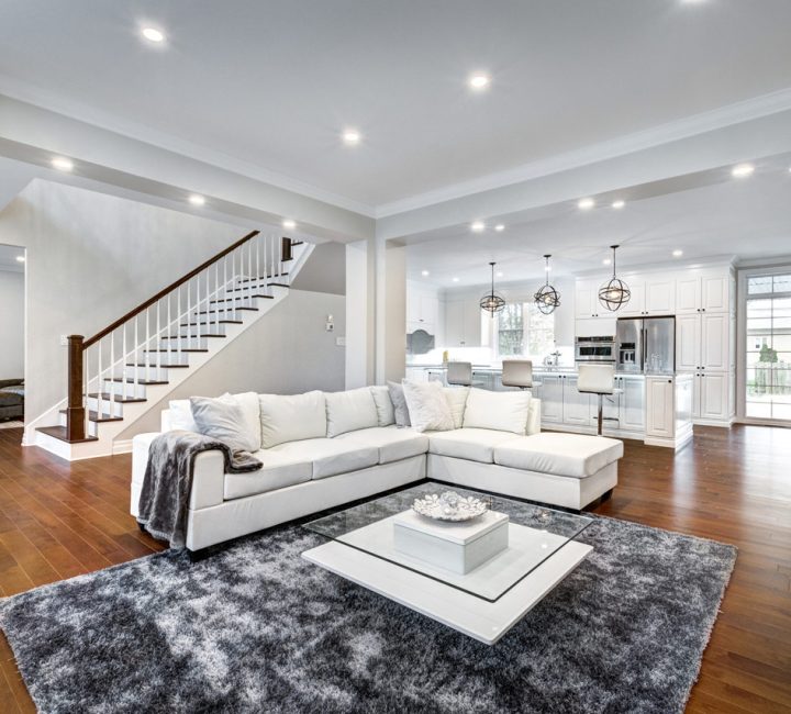 A spacious living area with white furniture, recessed ceiling lights, and an open view to the kitchen, demonstrating modern and inviting home design.